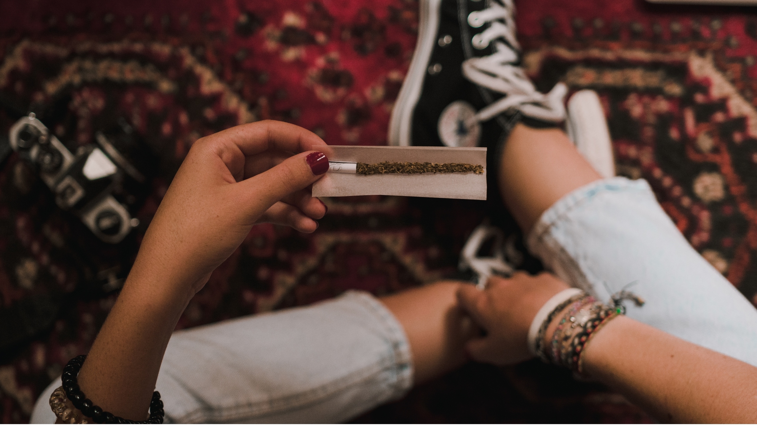 Plano subjetivo de un adolescente liando un cigarrillo de marihuana. Se ven, en primer plano, sus manos con el cigarrillo a medio liar.