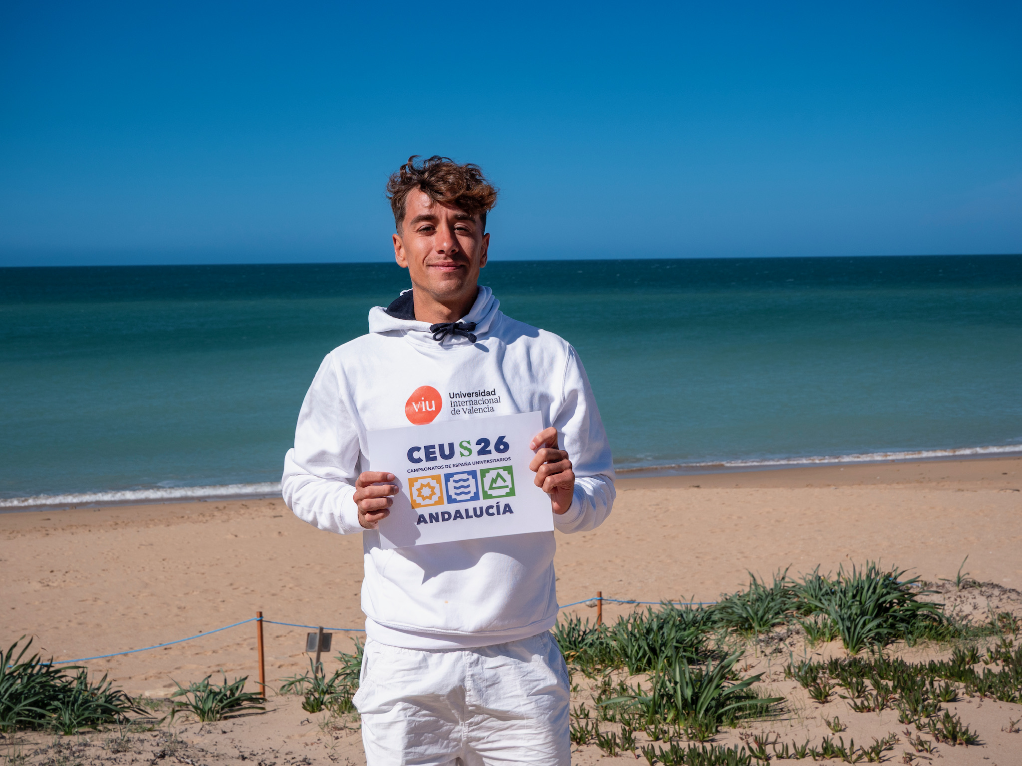 Iker Fernández, estudiante de VIU, con la playa de fondo, sosteniendo el con certificado del CEU Surf 2026 retrato