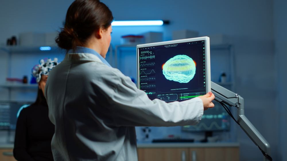 Una neuropsicóloga realiza un escáner cerebral a un paciente sentado junto a un monitor, mientras observa la imagen en pantalla