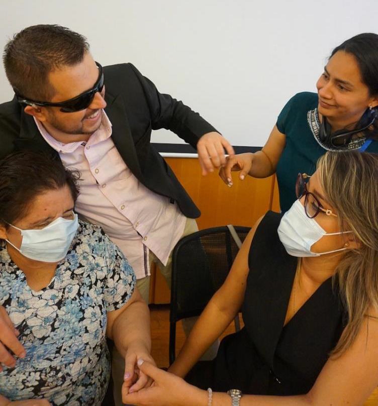 Un hombre y una mujer con sordoceguera (a la izquierda) se comunican entre sí con la ayuda de sus intérpretes-guías/intérpretes para sordociegos (a la derecha), utilizando la comunicación táctil. Fuente: WFBD