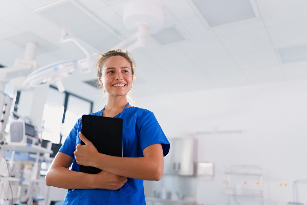 Profesional de enfermería gestionando el triaje hospitalario Una enfermera con uniforme azul sostiene una tableta digital en una unidad de triaje en enfermería hospitalaria.