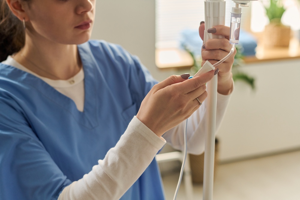 Personal de enfermería preparando una vía intravenosa en el servicio de urgencias Una profesional de la salud con uniforme médico azul ajusta el sistema de goteo de un suero intravenoso durante un proceso de atención médica.