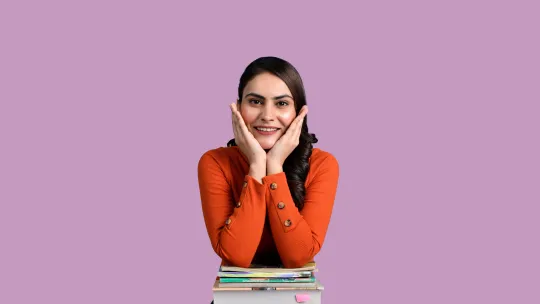 Estudiante joven sonriente apoyada sobre un bloque de libros, representando la preparación académica para la especialidad en el Máster de Profesorado.
