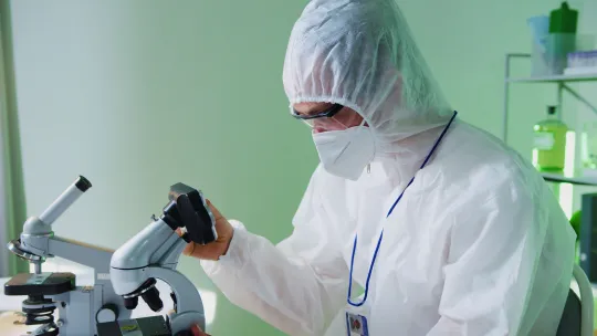 Investigador analizando muestras en el laboratorio bioinformático Científico con traje de protección biológica blanco, mascarilla y gafas de seguridad observando una muestra a través de un microscopio en un laboratorio.