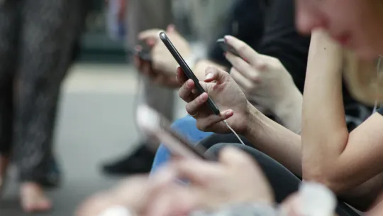 Personas utilizando sus teléfonos inteligentes en redes sociales adictivas Varias personas sentadas juntas mirando fijamente y utilizando sus teléfonos móviles con atención, en una escena que ilustra el uso continuo de redes sociales adictivas.
