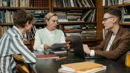 docente-con-gafas-orientando-a-dos-estudiantes-sobre-las-salidas-del-master-de-profesorado-en-una-biblioteca