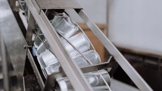 Línea industrial con software de automatización de procesos Latas metálicas de aluminio deslizándose en diagonal a través de un carril de cinta transportadora de acero en una planta industrial, ejemplificando el control del software de automatización de procesos.