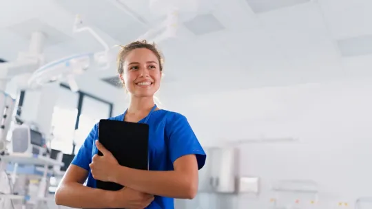 Una enfermera con uniforme azul sostiene una tableta digital en una unidad de triaje en enfermería hospitalaria.