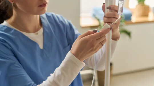 Personal de enfermería preparando una vía intravenosa en el servicio de urgencias Una profesional de la salud con uniforme médico azul ajusta el sistema de goteo de un suero intravenoso durante un proceso de atención médica.