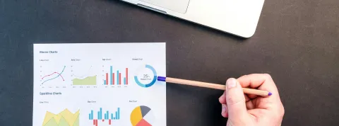 mano-sosteniendo-un-lapiz-que-senala-graficos-de-rendimiento-y-calidad-junto-a-un-ordenador-portatil