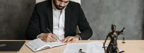 hombre-joven-escribiendo-sobre-documentos-legales-en-una-oficina-como-representacion-de-estudiar-abogacia