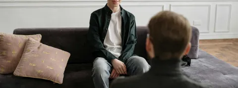 un-joven-en-una-sesion-con-un-neuropsicologo-sentado-en-un-sofa-gris