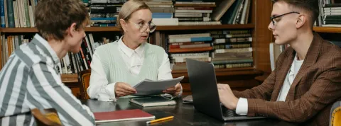 docente-con-gafas-orientando-a-dos-estudiantes-sobre-las-salidas-del-master-de-profesorado-en-una-biblioteca