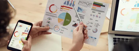 manos-de-personas-viendo-estadisticas-mediante-un-portatil-movil-y-papel-ejemplo-de-como-las-tic-en-colombia-impulsan-el-desarrollo-digital