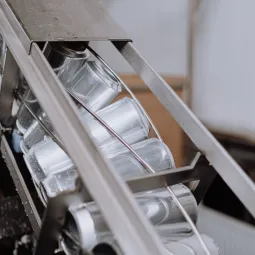Latas metálicas de aluminio deslizándose en diagonal a través de un carril de cinta transportadora de acero en una planta industrial, ejemplificando el control del software de automatización de procesos.