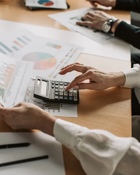 Persona en una mesa de oficina analizando informes financieros impresos con gráficos y utilizando una calculadora.