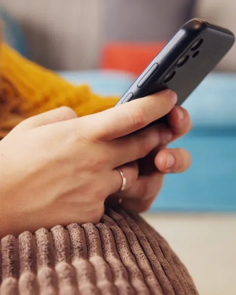 Primer plano de las manos de una mujer usando un teléfono móvil, apoyada en un cojín de color marrón, relacionando la tecnología digital con la empatía y la inteligencia artificial.