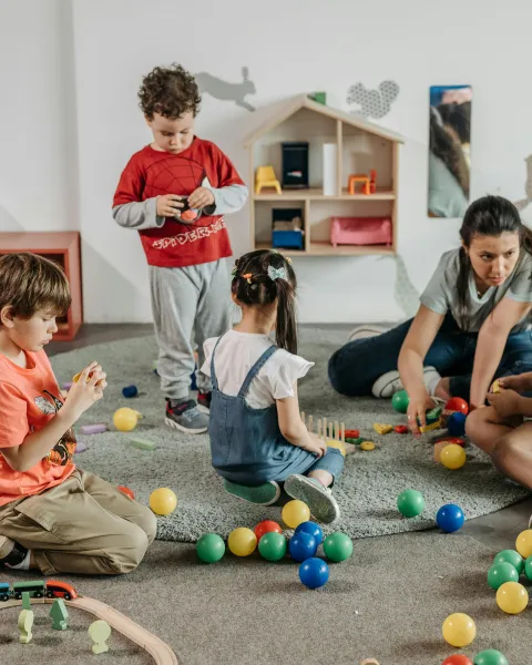 Niños jugando con pelotas y juguetes de madera junto a su profesora en un entorno de juego inclusivo para niños.