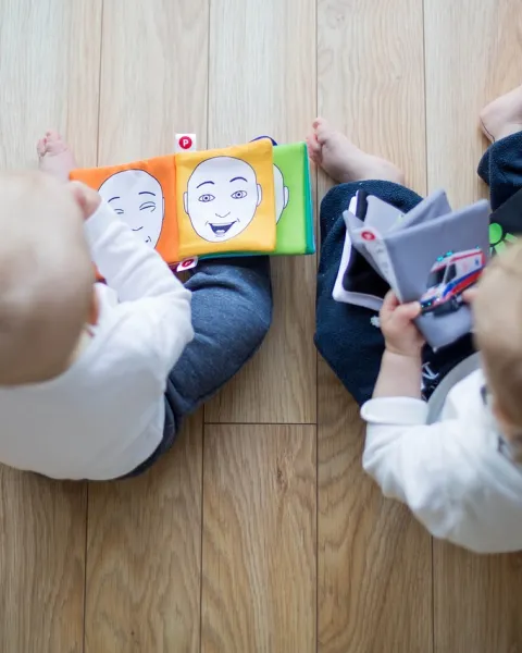 plano-cenital-de-dos-bebes-sentados-en-el-suelo-jugando-con-libros-infantiles-a-los-cuales-les-estan-haciendo-estudios-sobre-neuropsicologia-infantil