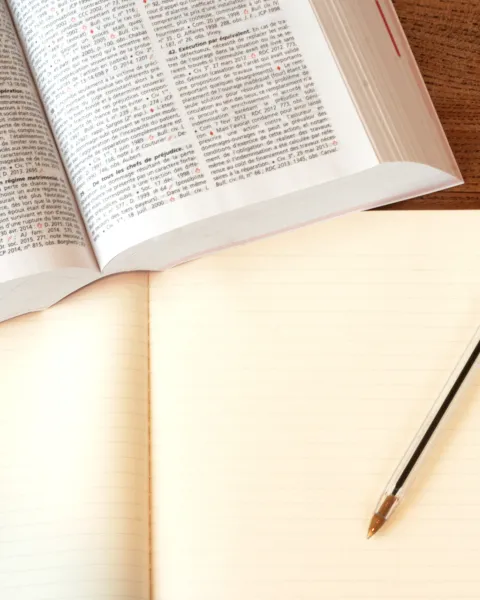Libro de texto jurídico abierto sobre una mesa de madera junto a un cuaderno en blanco y un bolígrafo azul, simbolizando el estudio para las oposiciones de derecho.