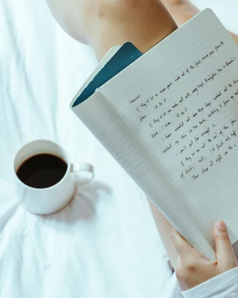 persona-escribiendo-en-una-libreta-sobre-la-cama-con-una-taza-de-cafe-representando-el-proceso-de-ser-escritor