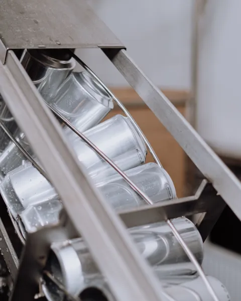 Latas metálicas de aluminio deslizándose en diagonal a través de un carril de cinta transportadora de acero en una planta industrial, ejemplificando el control del software de automatización de procesos.