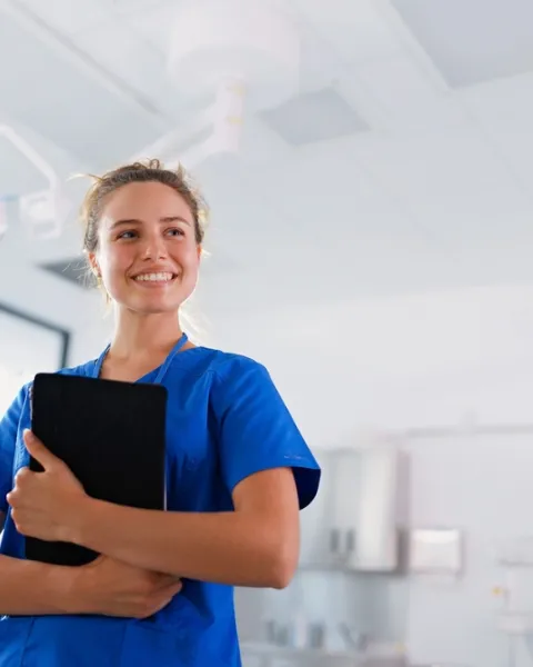 Una enfermera con uniforme azul sostiene una tableta digital en una unidad de triaje en enfermería hospitalaria.
