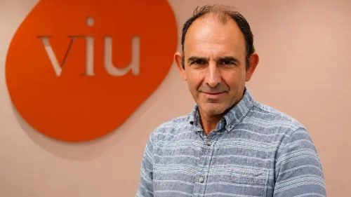 Retrato del experto de VIU Raúl Reyero. Viste camisa a rayas azul y en el fondo del retrato se encuentra el logo de VIU